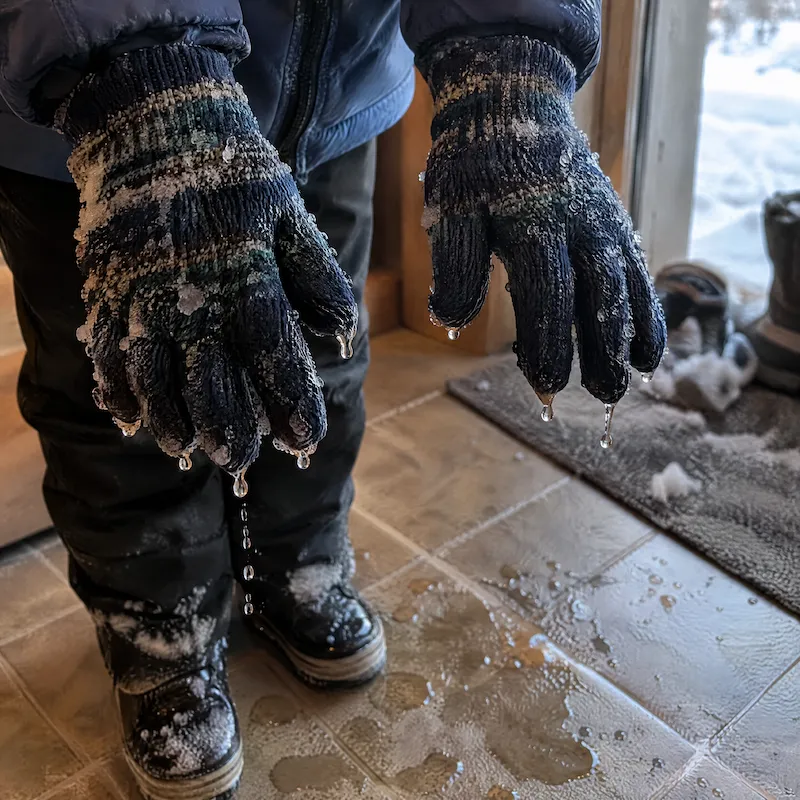 Small children's hands in soaked, frozen yarn gloves dripping onto a floor